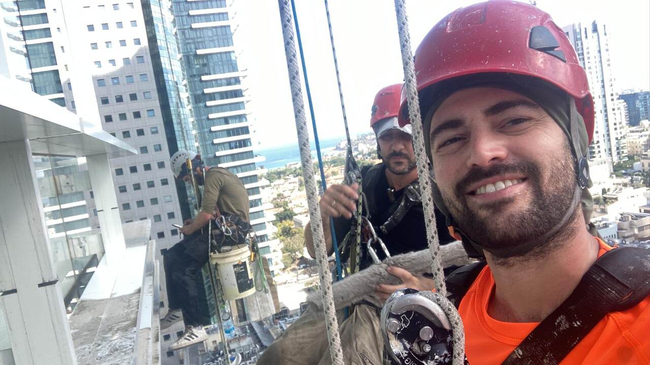עובד גולש מצויד ברתמת בטיחות לעבודות גובה על חזית בניין
